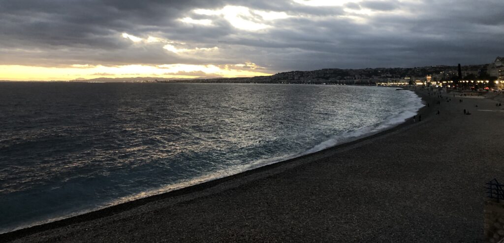 La plage et la baie des Anges à Nice, sous un ciel nuageux éclairé par le soleil.